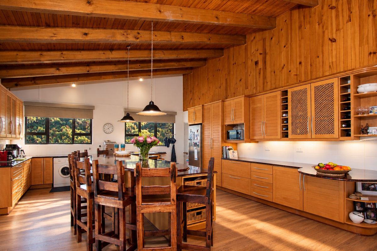 Spacious kitchen featuring warm timber-clad vaulted ceilings, exposed beams, extensive fitted cabinetry, stone countertops, and integrated appliances in a bright, open-plan layout.