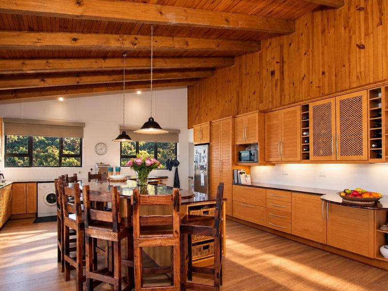 Spacious kitchen featuring warm timber-clad vaulted ceilings, exposed beams, extensive fitted cabinetry, stone countertops, and integrated appliances in a bright, open-plan layout.
