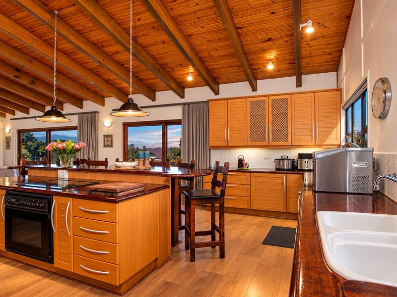 Spacious kitchen featuring a vaulted timber-clad ceiling with exposed beams, wooden cabinetry, a large central island, and modern integrated appliances.