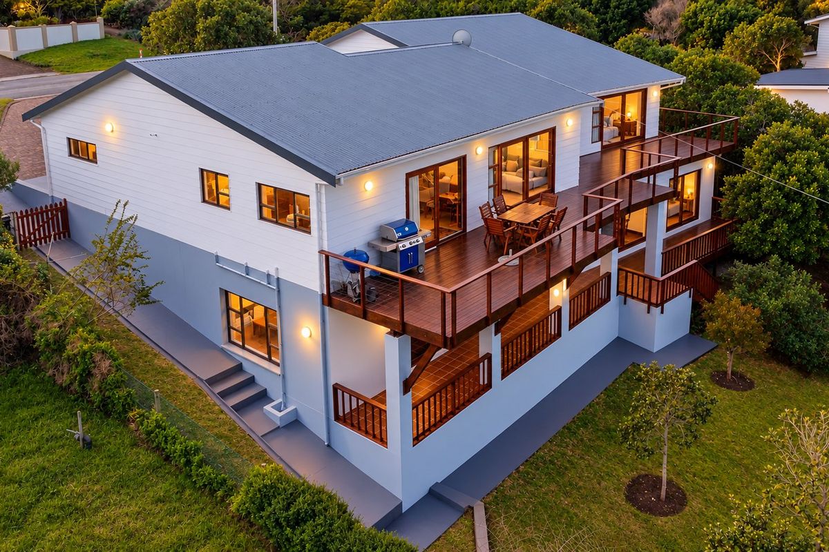 Aerial view of a two-story house featuring a large elevated timber deck, sliding glass doors, and a well-maintained exterior with a metal roof.