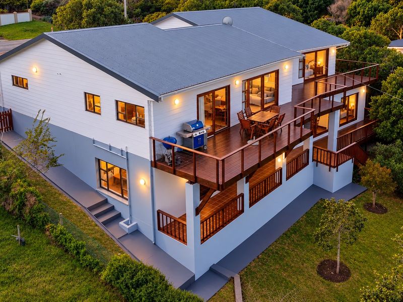 Aerial view of a two-story house featuring a large elevated timber deck, sliding glass doors, and a well-maintained exterior with a metal roof.