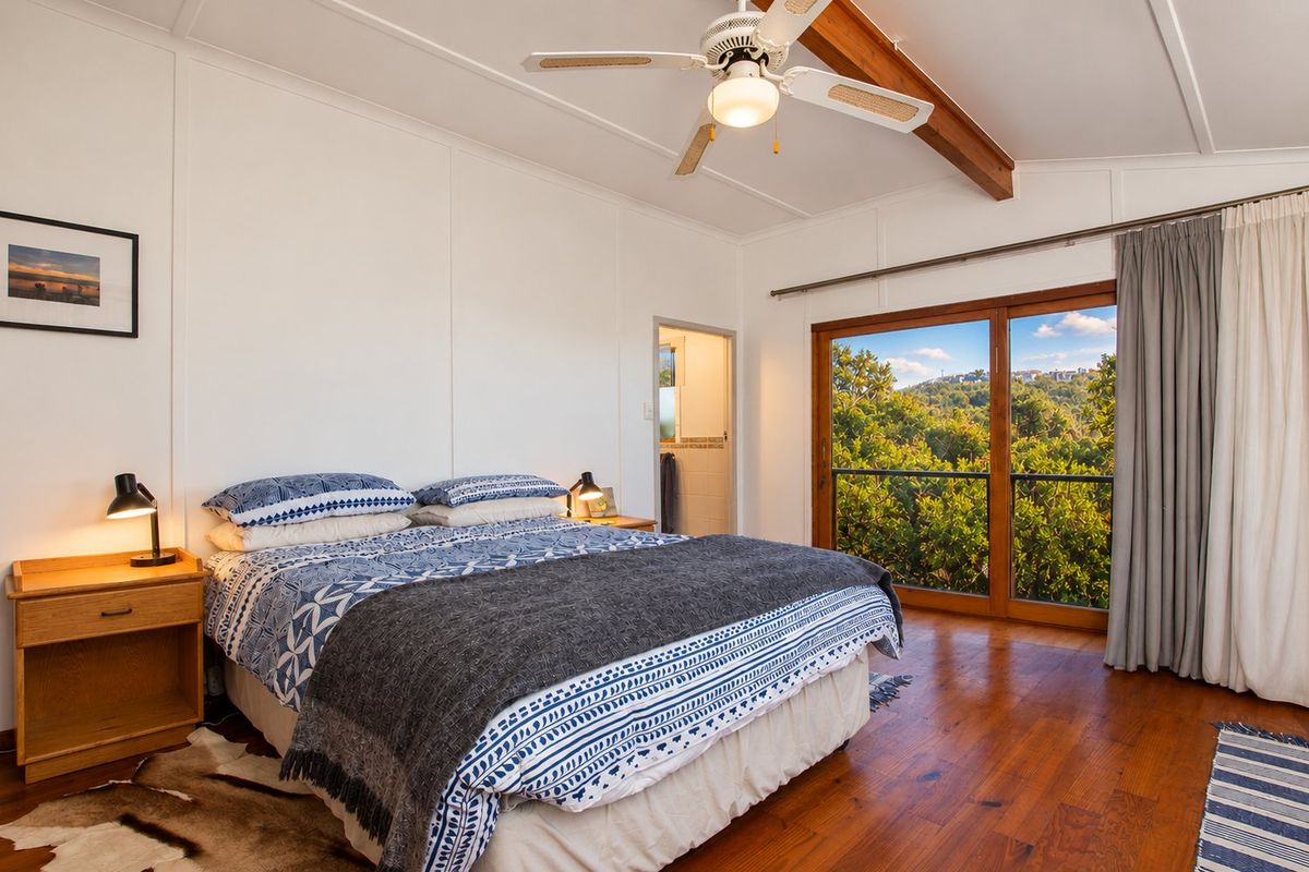 Spacious bedroom featuring polished timber flooring, exposed ceiling beam, ceiling fan, and large sliding glass doors opening to a scenic outdoor view.