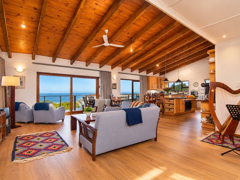 Spacious open-plan living and kitchen area featuring high exposed timber beam ceilings, laminate flooring, and large sliding doors opening to a scenic ocean view.