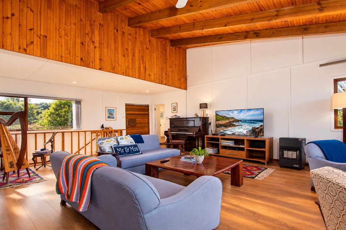 Spacious living room featuring high vaulted ceilings with exposed timber beams, warm timber wall paneling, and durable laminate flooring with a built-in gas heater.