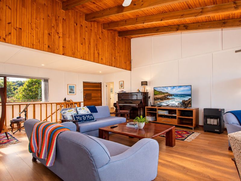 Spacious living room featuring high vaulted ceilings with exposed timber beams, warm timber wall paneling, and durable laminate flooring with a built-in gas heater.