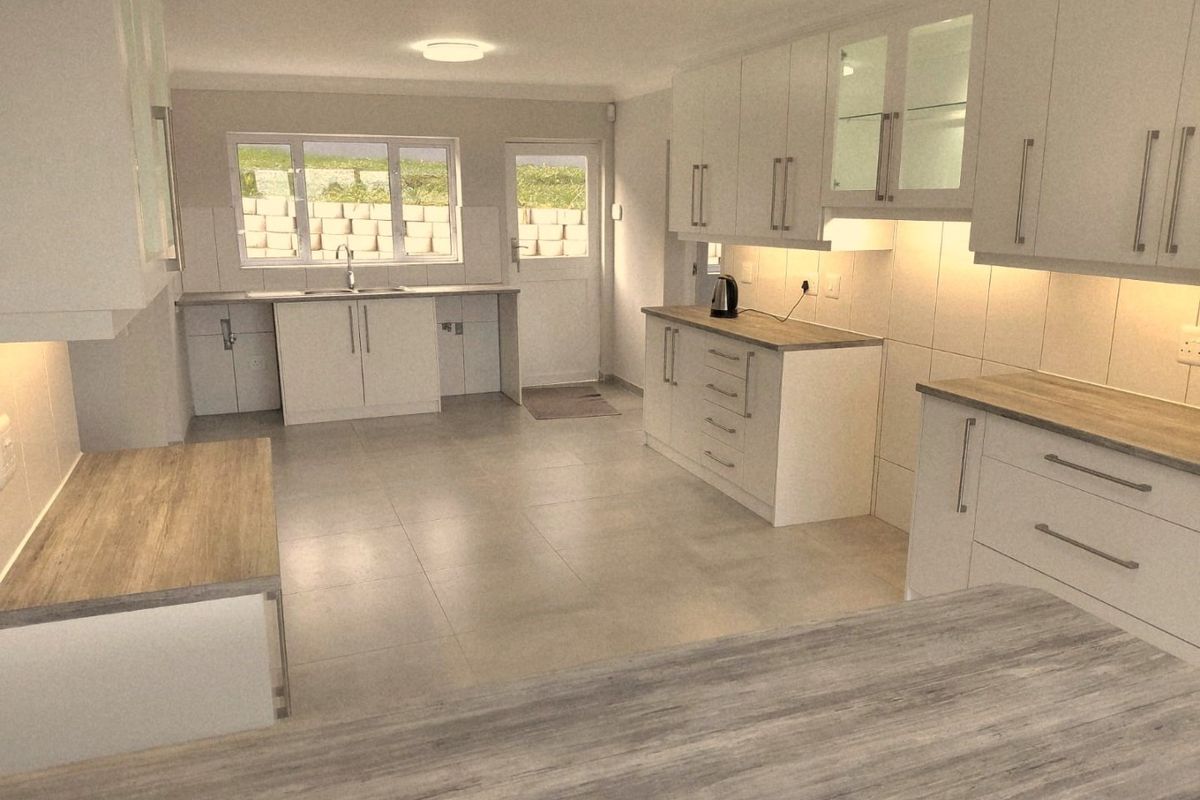 A clean, modern kitchen featuring white cabinetry, wood-look countertops, tiled flooring, and integrated lighting, offering a bright and functional workspace.