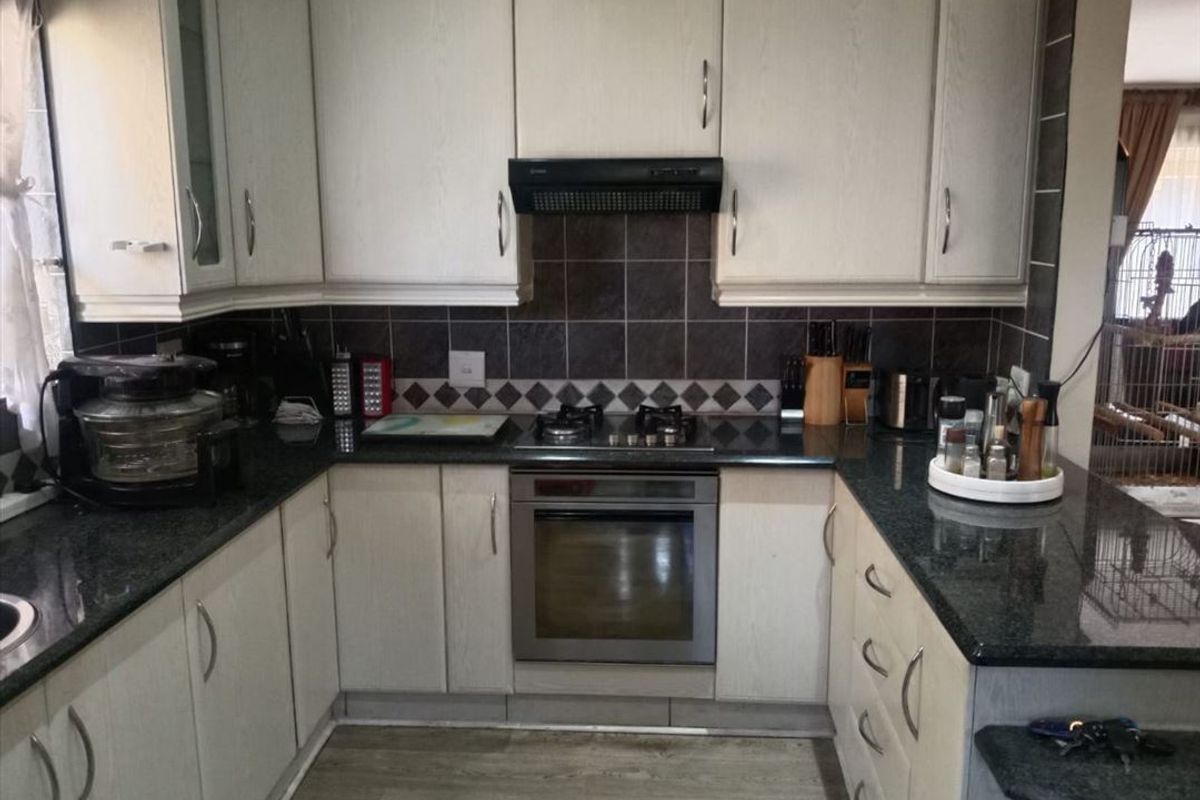 U-shaped kitchen featuring light-toned cabinetry, dark granite countertops, a built-in oven, gas hob, and extractor fan with tiled backsplash.