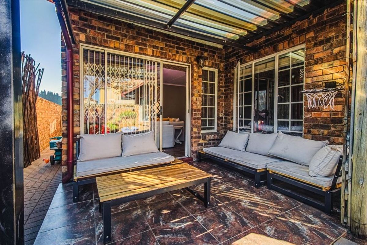A covered patio area featuring exposed brick walls, tiled flooring, and a translucent roof structure, providing a functional outdoor living space.