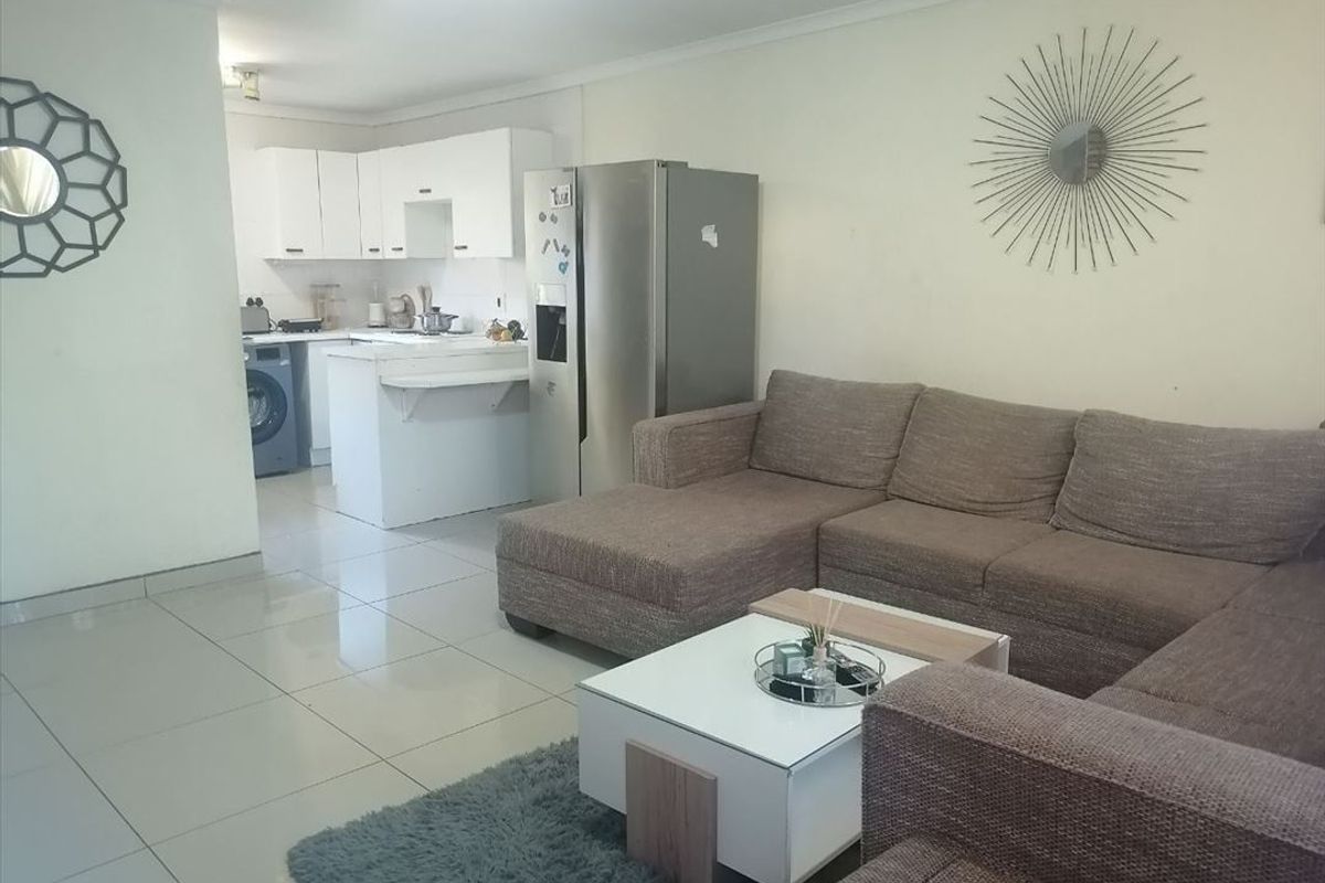 Open-plan living area featuring tiled flooring and a compact kitchen with white cabinetry, seamlessly flowing into the lounge space.