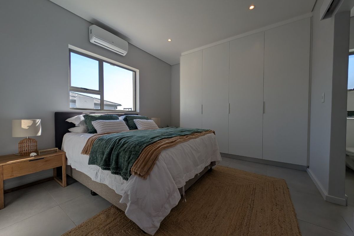 A modern, well-lit bedroom featuring built-in floor-to-ceiling wardrobes, tiled flooring, and a wall-mounted air conditioning unit.