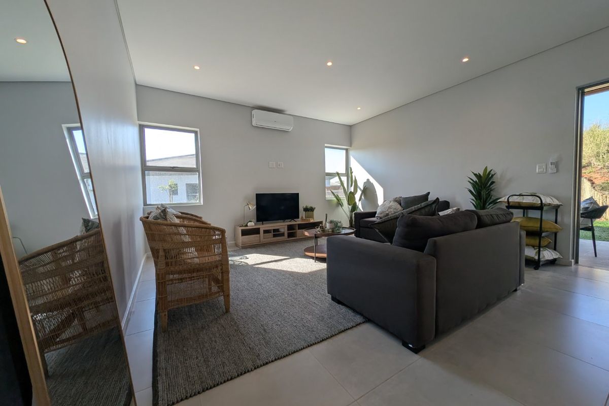 A bright and modern living room featuring tiled flooring, recessed lighting, and a wall-mounted air conditioning unit, with direct access to an outdoor area.
