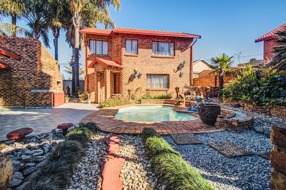 A two-story face-brick house featuring a swimming pool, paved patio area, and landscaped garden with stone pathways.