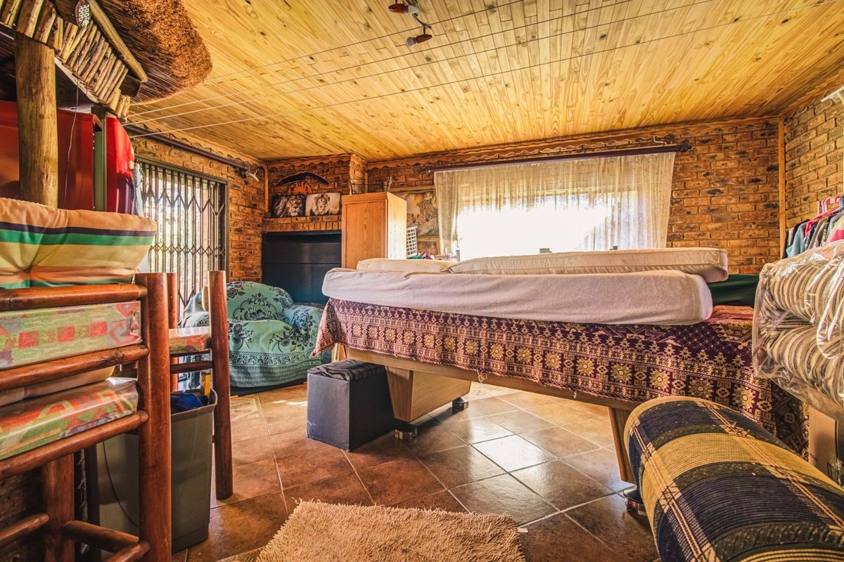 A rustic bedroom featuring exposed brick walls, a timber-clad ceiling, and tiled flooring, with access to an outdoor area through a security gate.