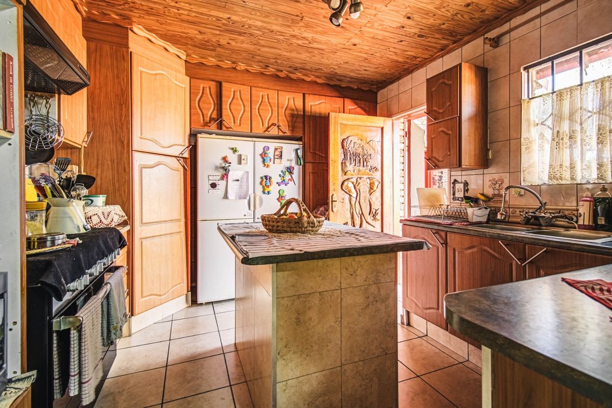 A traditional kitchen featuring timber cabinetry, a central island, tiled flooring, and a wood-paneled ceiling, offering a functional layout with classic finishes.
