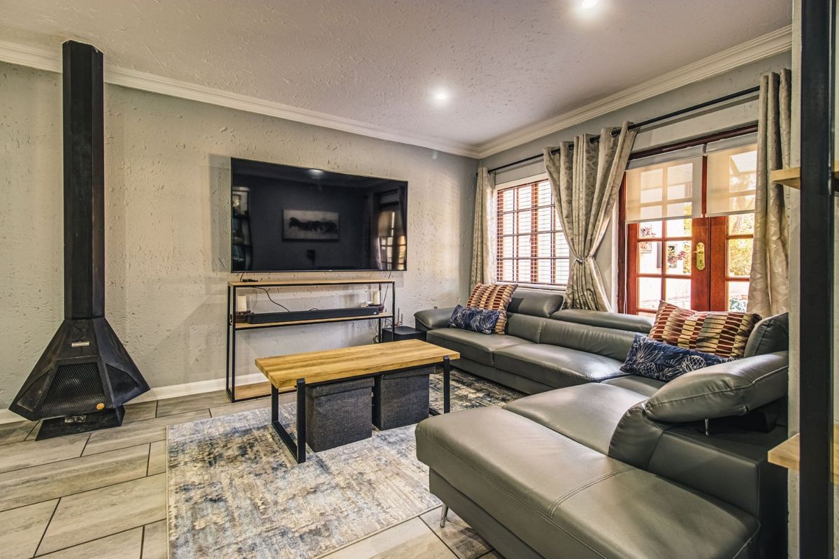 A comfortable living room featuring a modern freestanding fireplace, tiled flooring, crown molding, and direct access to the outdoors through classic french doors.