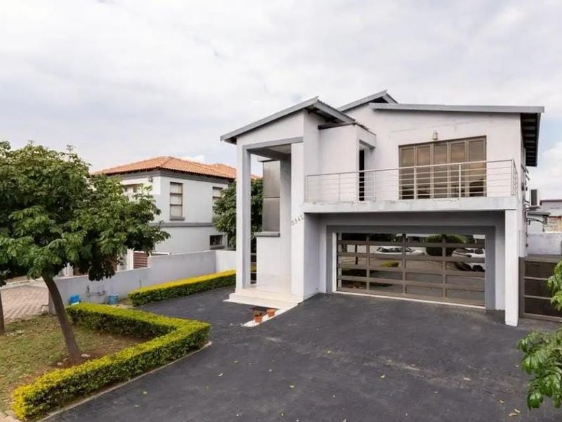 A modern two-story residential property featuring a paved driveway, integrated garage, and an upper-level balcony with metal railings.