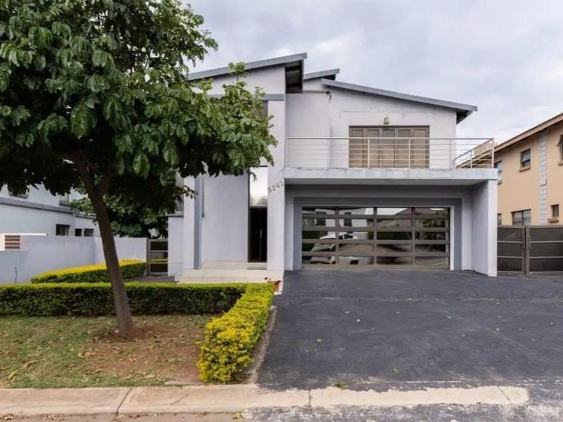Modern double-story residential property featuring a paved driveway, integrated garage, and an upper-level balcony with stainless steel railing.