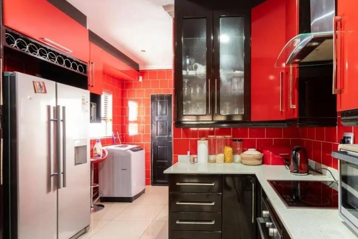 A vibrant kitchen featuring high-gloss red and black cabinetry, tiled walls, stone countertops, and integrated cooking appliances.