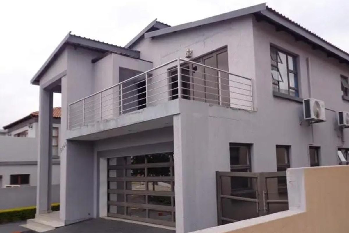 A modern two-story residential property featuring a double garage, a balcony with stainless steel railings, and exterior air conditioning units.