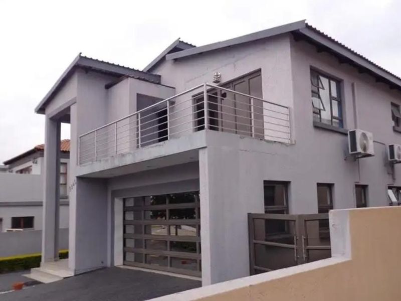 A modern two-story residential property featuring a double garage, a balcony with stainless steel railings, and exterior air conditioning units.