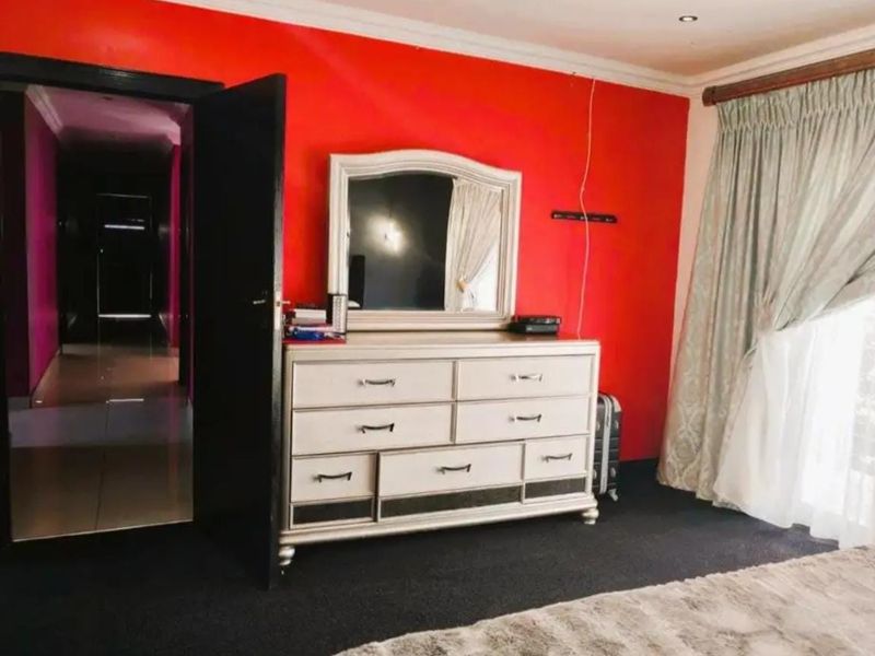 A bedroom featuring dark carpeting, a bold red accent wall, and a doorway leading to a hallway.