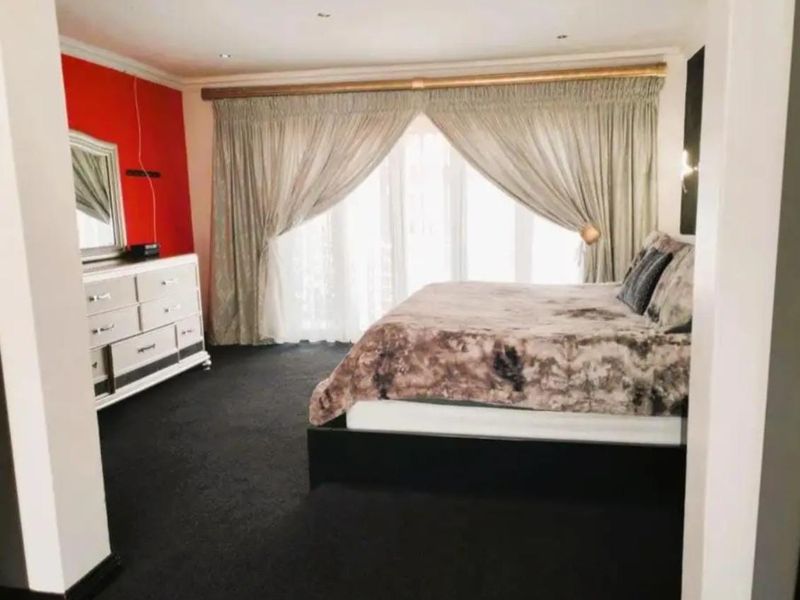 Spacious bedroom featuring dark carpeting, recessed ceiling lighting, and large sliding glass doors with curtains providing access to the exterior.