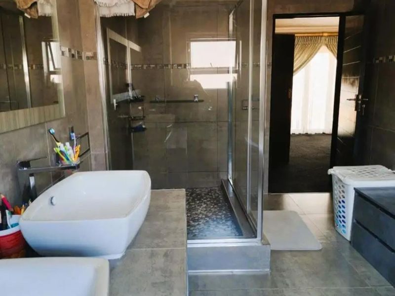 Modern bathroom featuring dual vessel sinks on a tiled vanity, a glass-enclosed shower with pebble-style flooring, and neutral wall tiling.