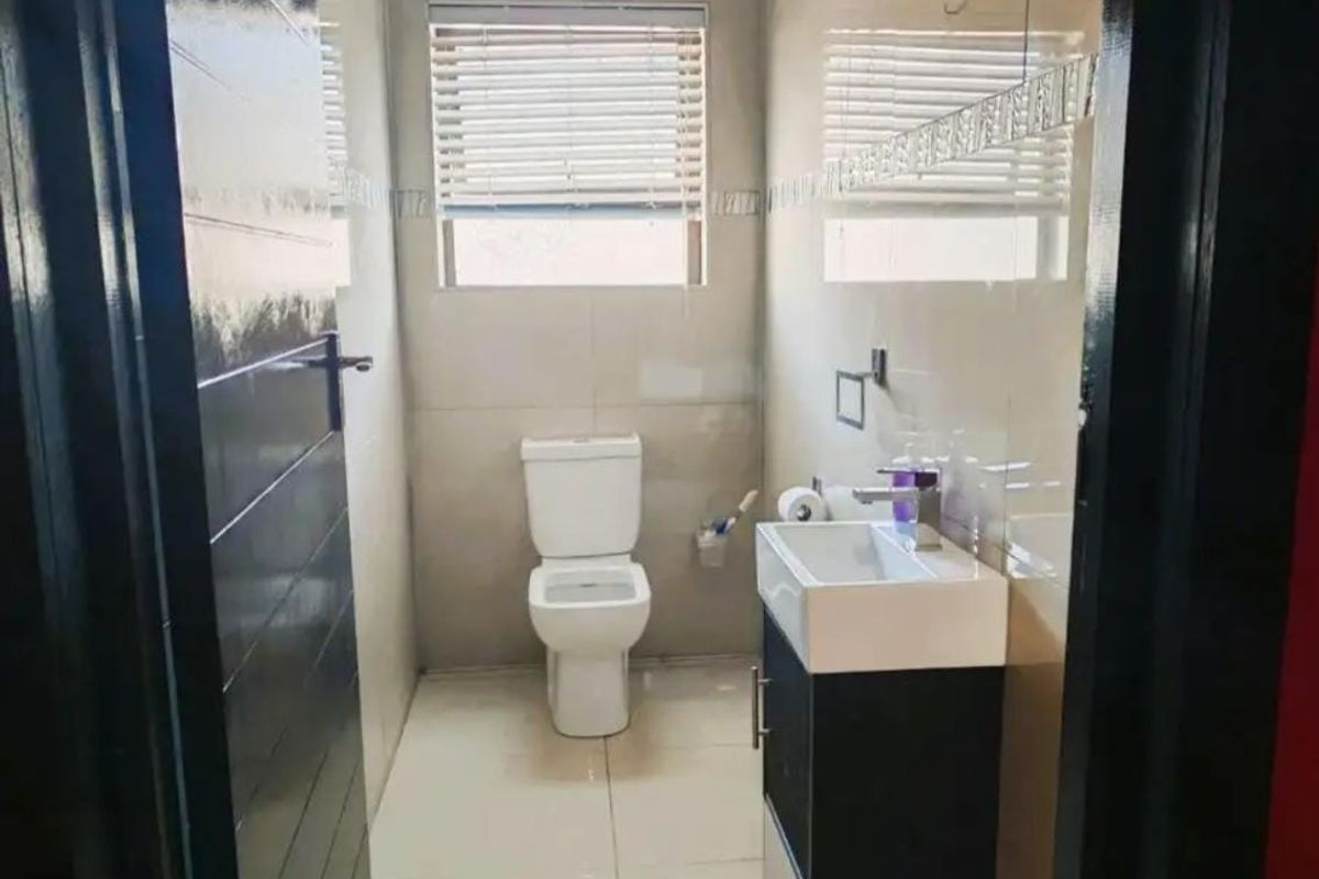 A modern, compact bathroom featuring tiled walls and floors, a wall-mounted vanity with a basin, and a standard toilet.