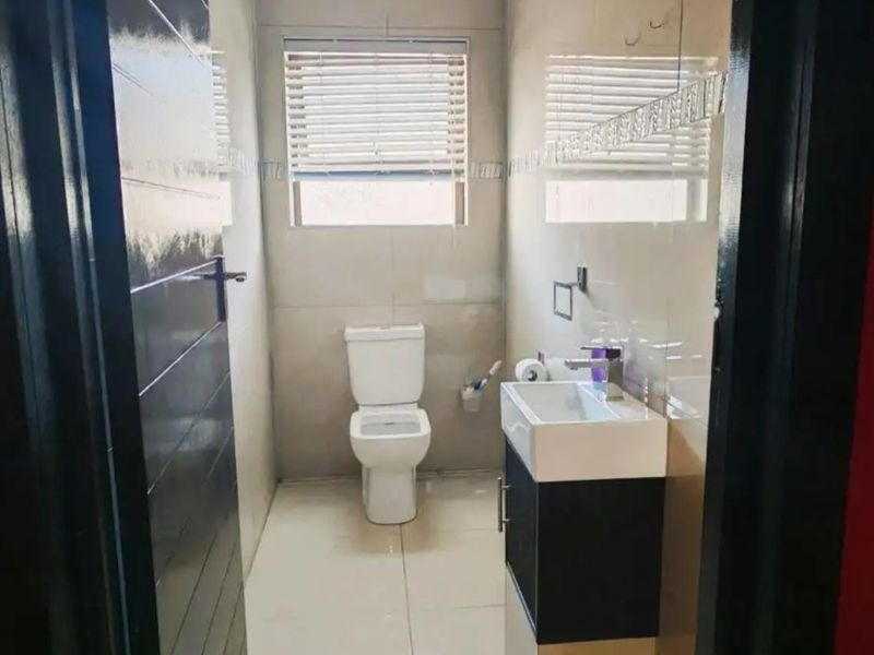 A modern, compact bathroom featuring tiled walls and floors, a wall-mounted vanity with a basin, and a standard toilet.