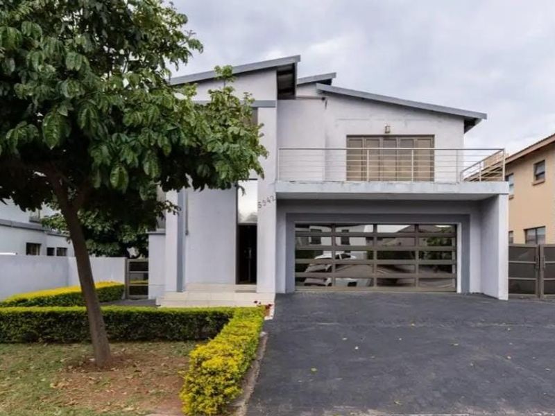 A modern two-story residential property featuring a double garage, balcony with metal railing, and a paved driveway with a landscaped front garden.