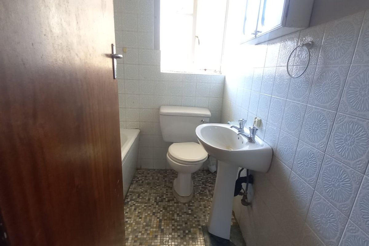A compact bathroom featuring a pedestal basin, toilet, and bathtub with dated wall and floor tiling, requiring modernization.
