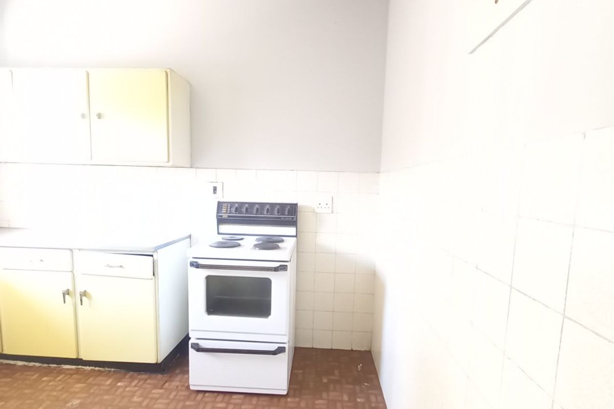 A dated kitchen featuring original cabinetry, a freestanding stove, and tiled splashbacks, offering a blank canvas for potential renovation and modernization.