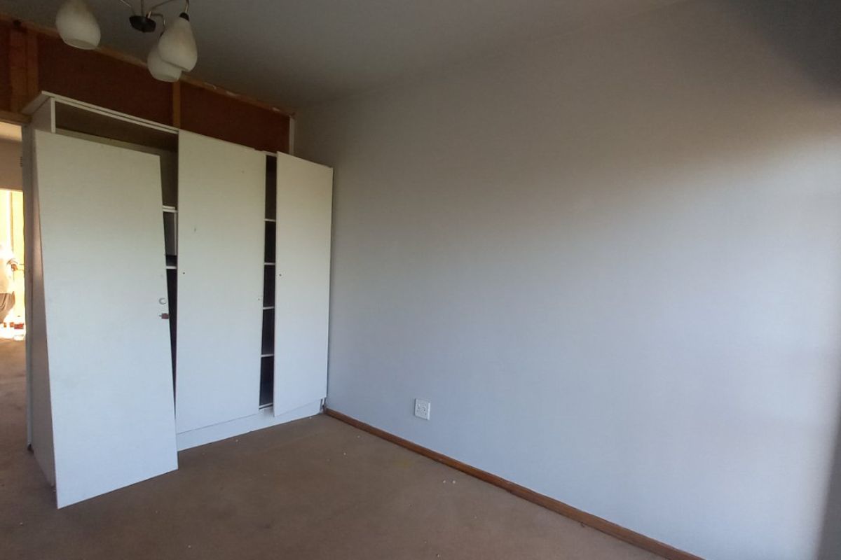 A bedroom featuring built-in wardrobes with an unfinished bulkhead area, neutral wall finishes, and carpet flooring.