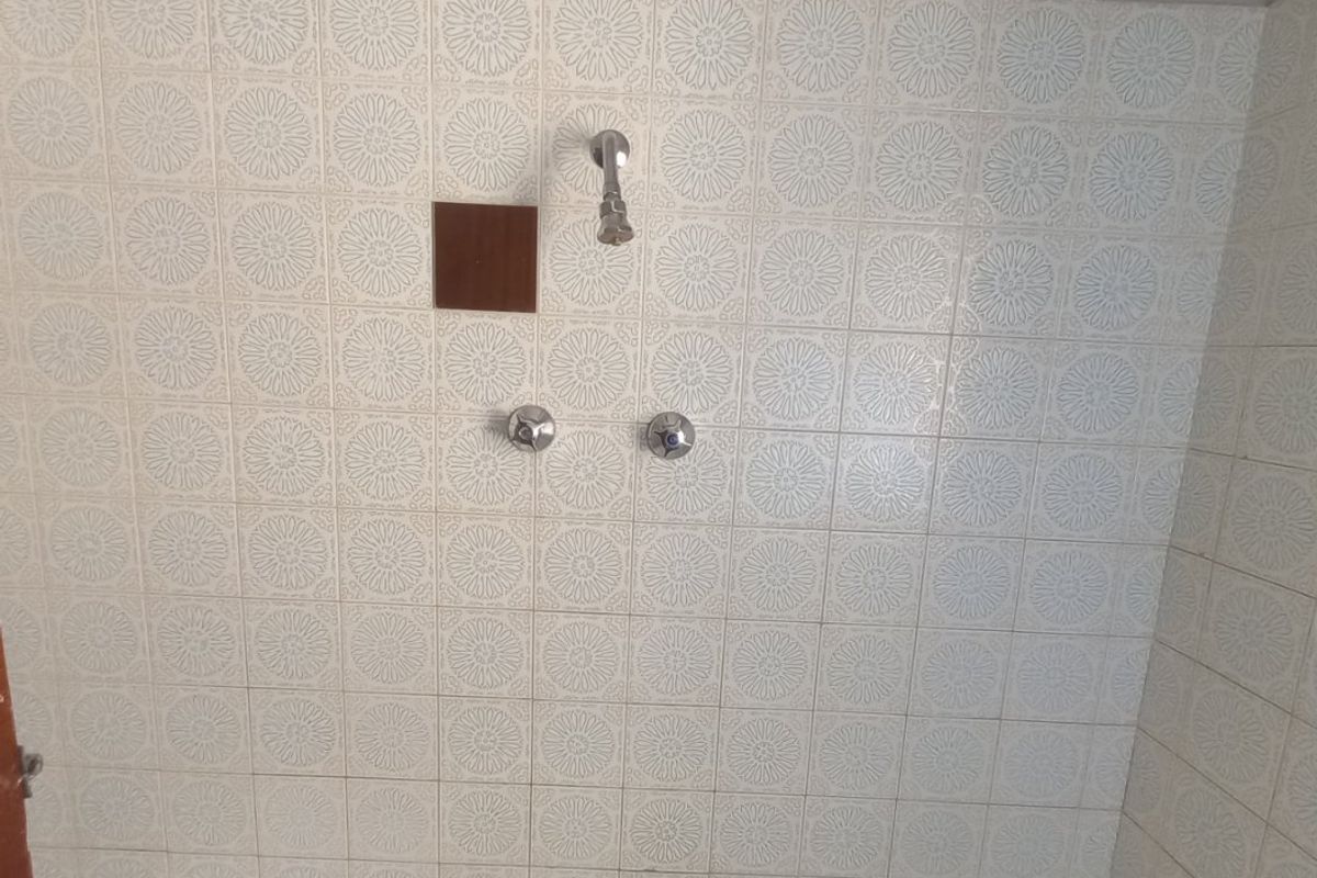 A dated bathroom shower and bathtub area featuring patterned wall tiles and original chrome plumbing fixtures.