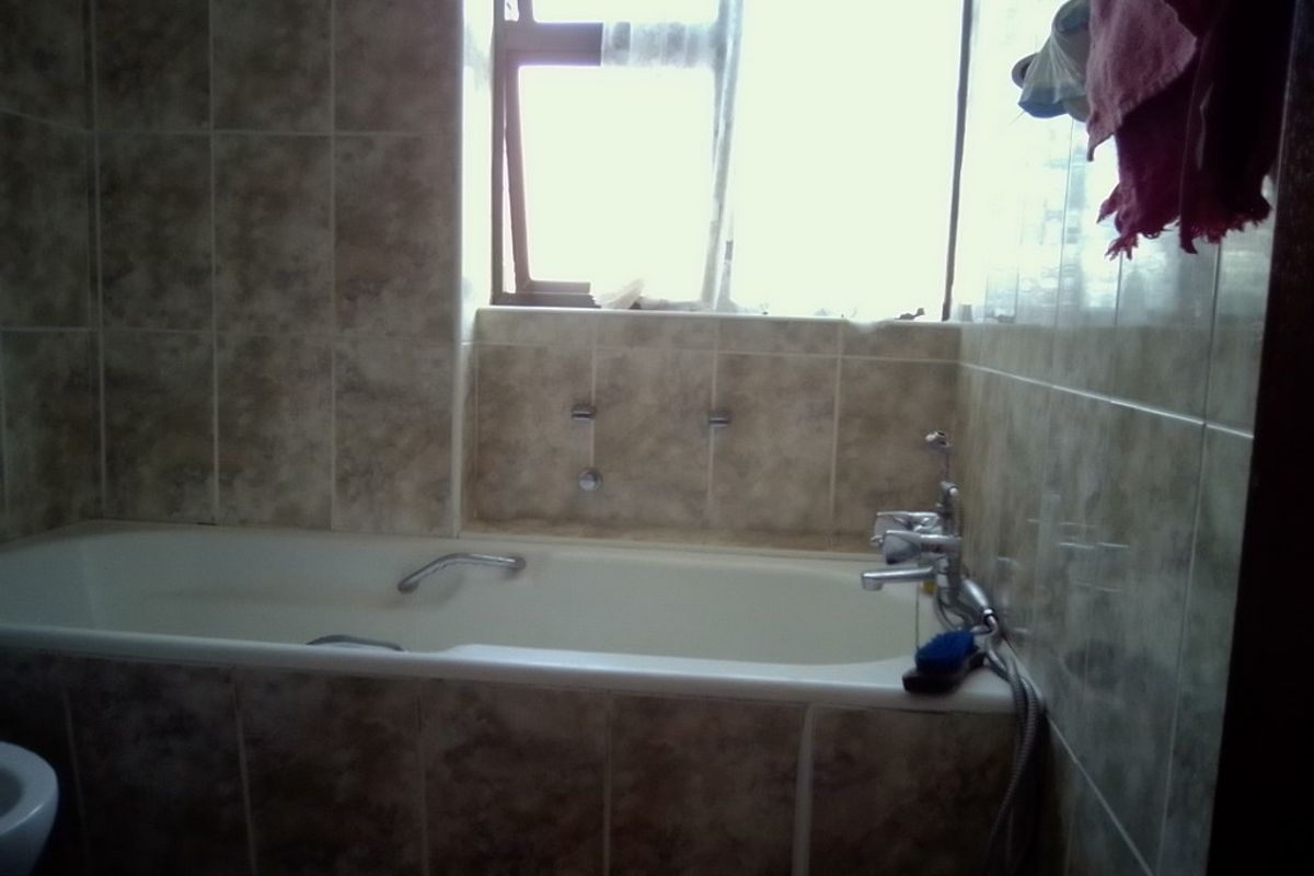 A functional bathroom featuring a built-in bathtub with chrome mixer tap and shower attachment, finished with neutral wall tiling.