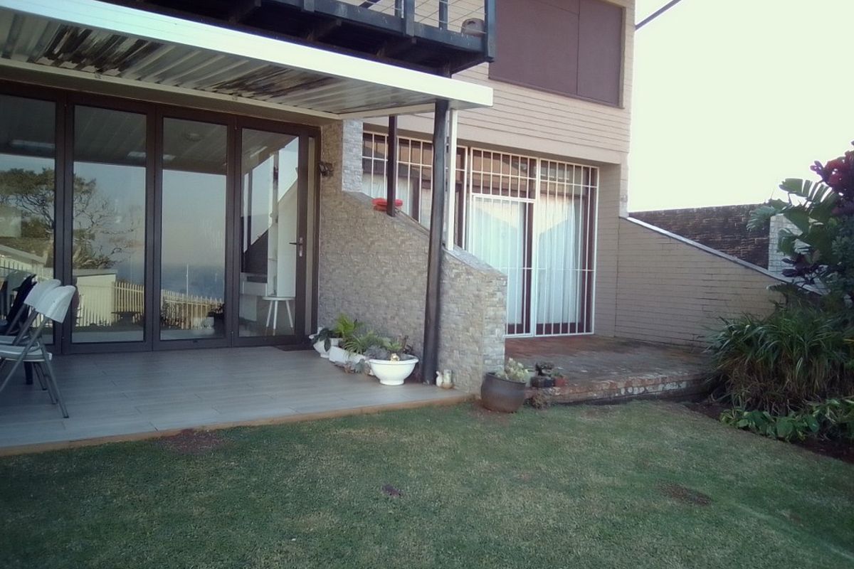 Rear view of the townhouse featuring a covered patio area, tiled flooring, stone-clad feature wall, and access to a private garden space.