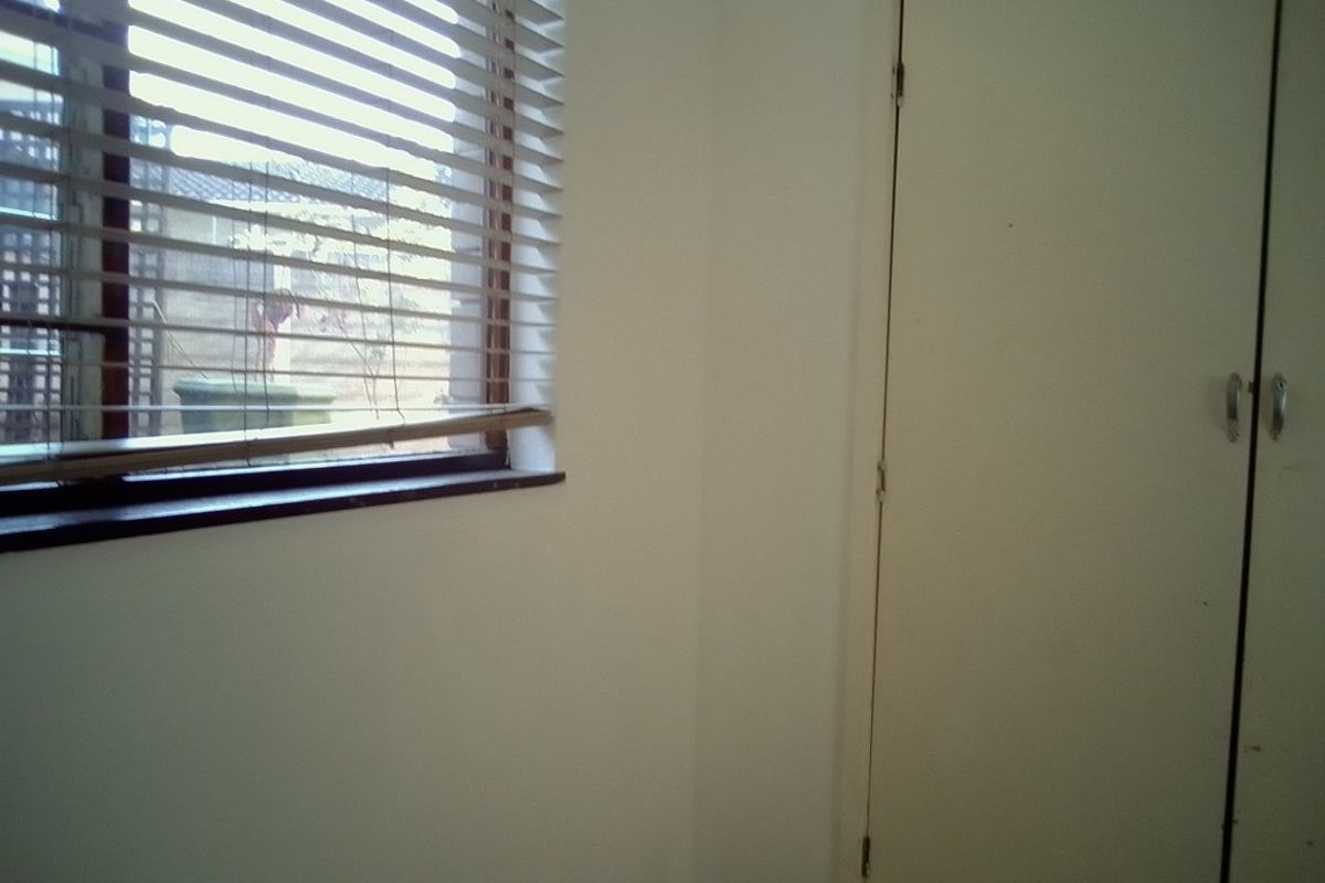 A bedroom interior featuring a built-in cupboard and a window with horizontal blinds, showing signs of wear and requiring cosmetic updates.