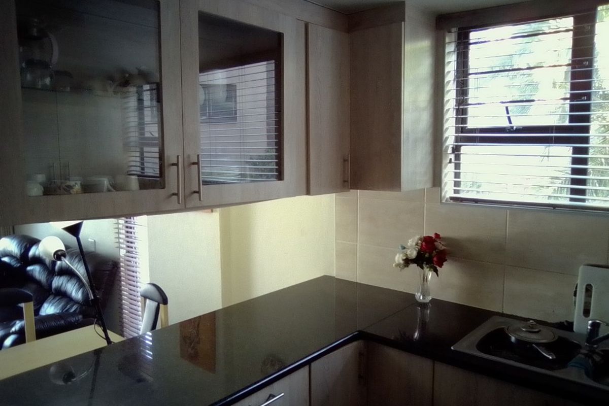 A functional kitchen featuring light wood cabinetry, dark granite countertops, tiled splashbacks, and a window with fitted blinds.
