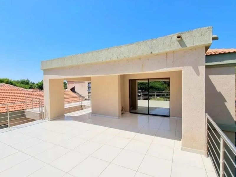 A spacious covered balcony featuring tiled flooring, stainless steel railings, and sliding glass door access to the interior living space.