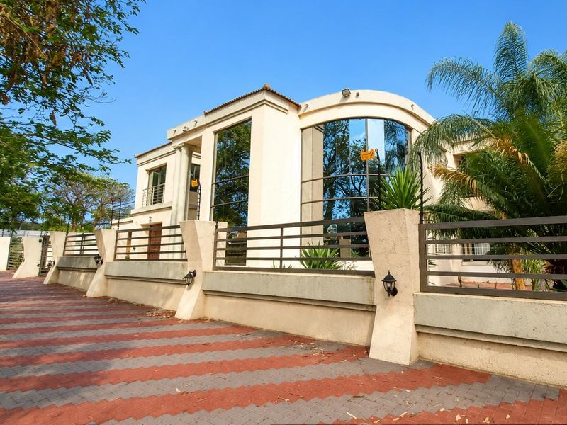 A modern multi-story residence featuring a curved glass facade, paved driveway, and secure perimeter wall with integrated lighting.