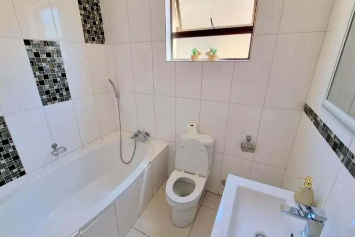 A functional bathroom featuring a built-in bathtub with handheld shower, a modern basin with chrome mixer, and a standard toilet.