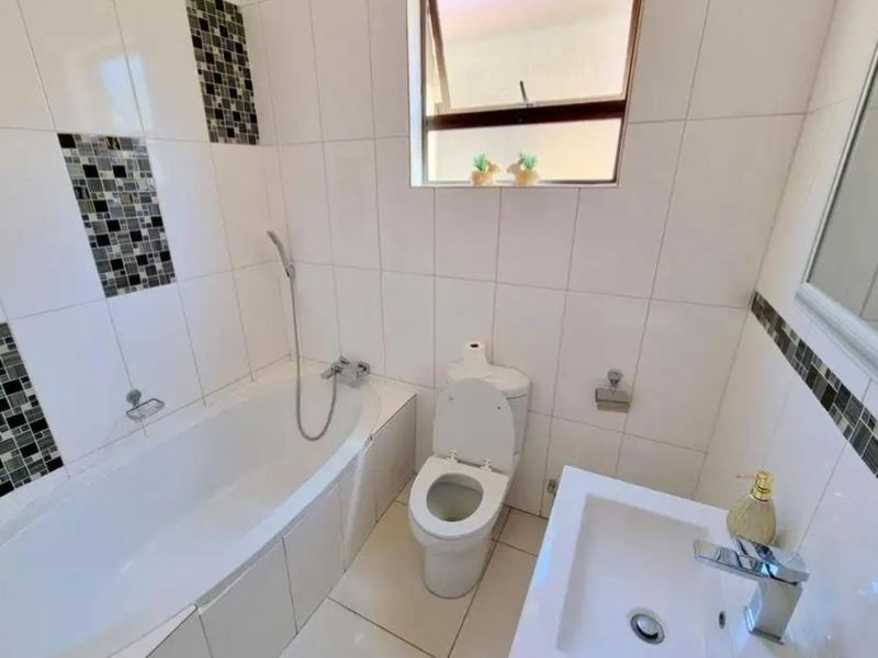 A functional bathroom featuring a built-in bathtub with handheld shower, a modern basin with chrome mixer, and a standard toilet.