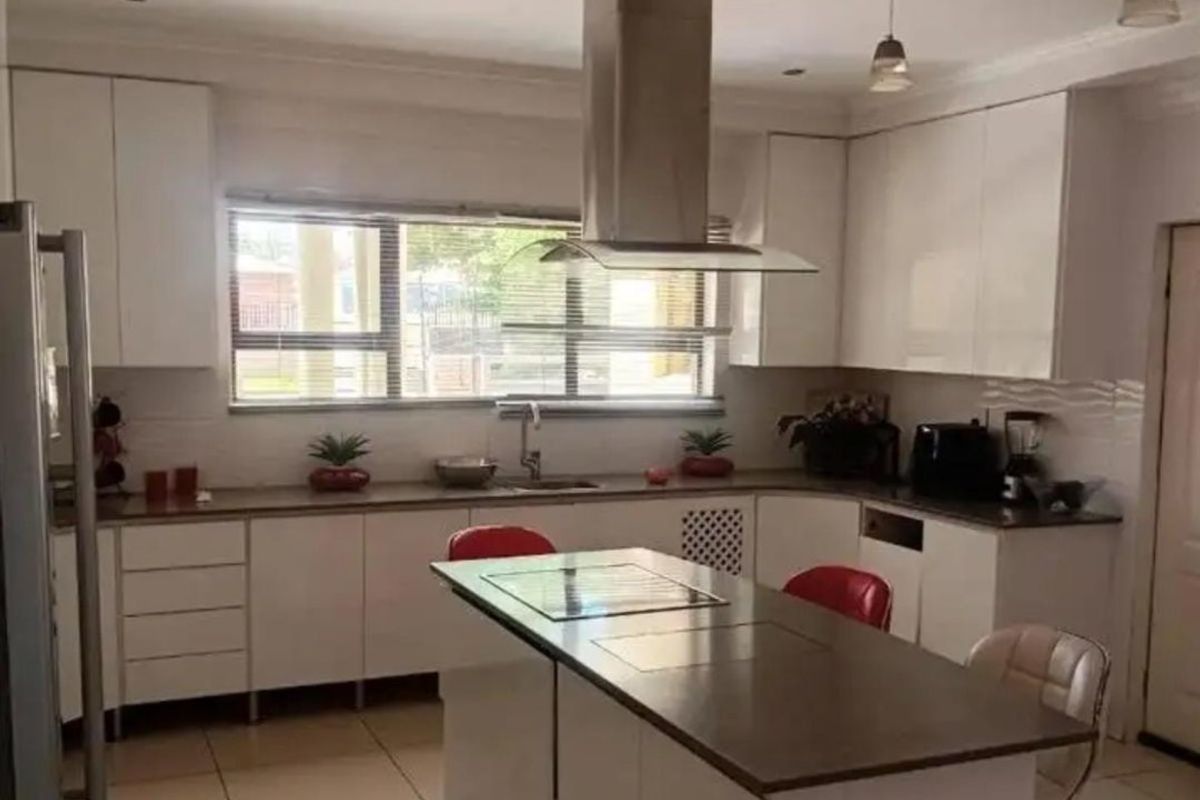 A modern kitchen featuring white cabinetry, a central island with a built-in hob, stainless steel extractor fan, and tiled flooring.