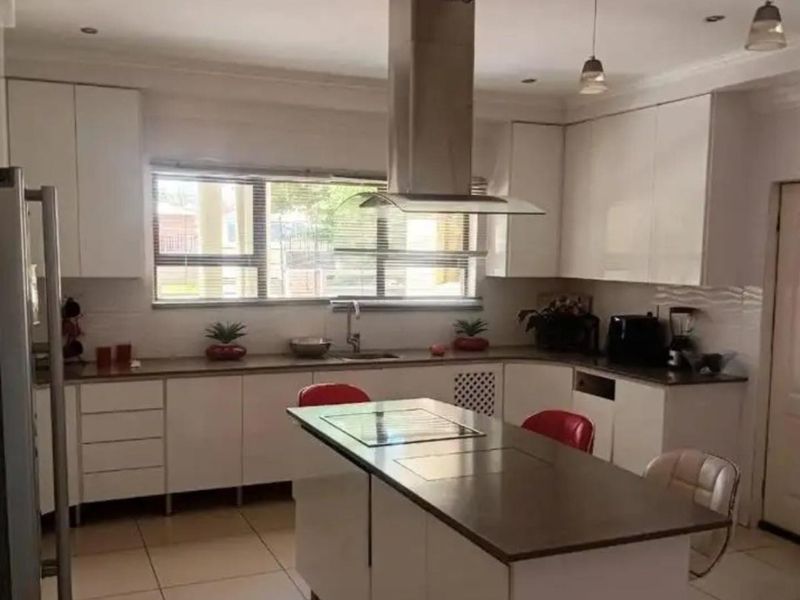 A modern kitchen featuring white cabinetry, a central island with a built-in hob, stainless steel extractor fan, and tiled flooring.