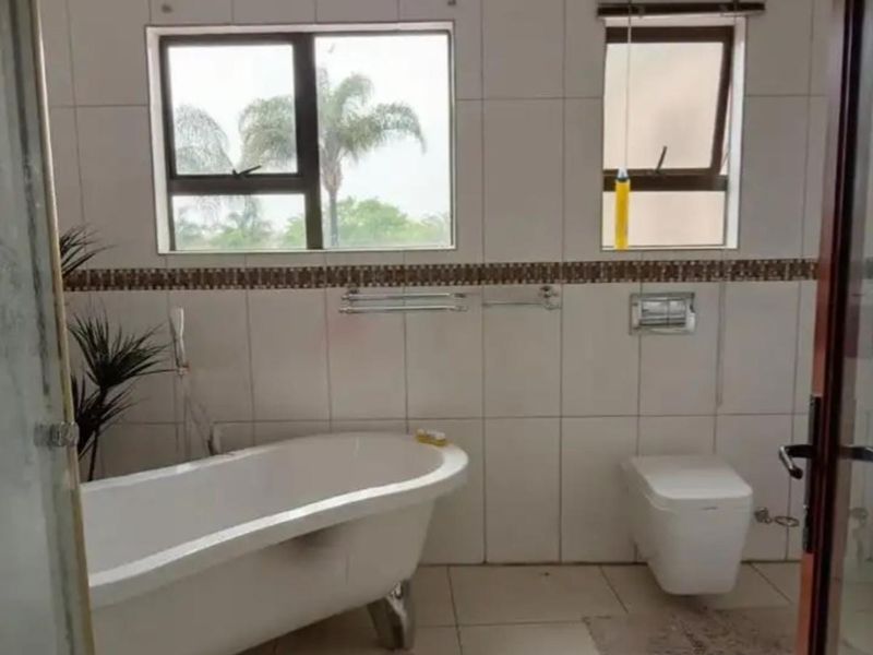 A functional bathroom featuring a freestanding bathtub, wall-mounted toilet, and tiled walls with a decorative border.