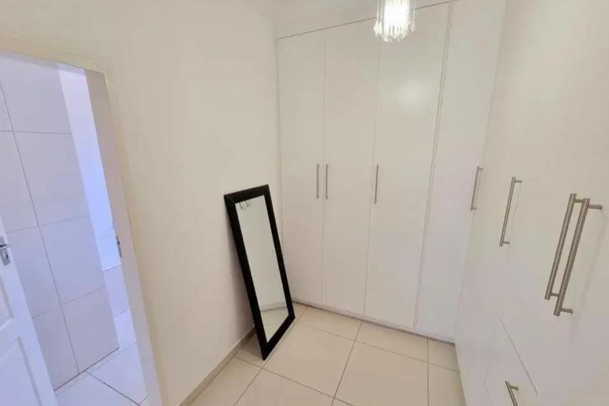 A clean and bright dressing area featuring floor-to-ceiling built-in wardrobes with modern white cabinetry and tiled flooring.