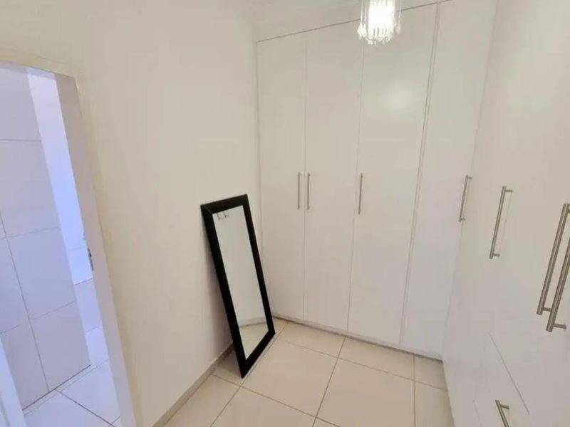 A clean and bright dressing area featuring floor-to-ceiling built-in wardrobes with modern white cabinetry and tiled flooring.