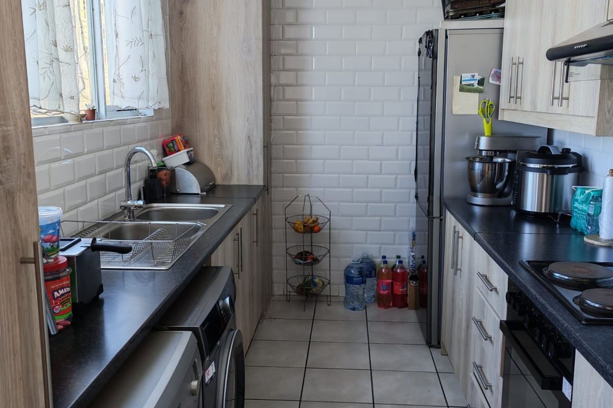 A functional galley-style kitchen featuring light wood-grain cabinetry, subway tile backsplash, dark countertops, and integrated space for laundry appliances.