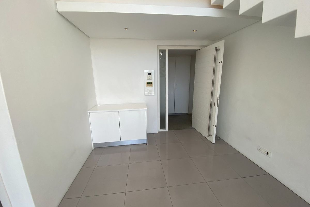 A clean, modern entry area featuring tiled flooring, recessed ceiling lighting, a built-in cabinet, and a secure entrance door leading to an adjacent room.