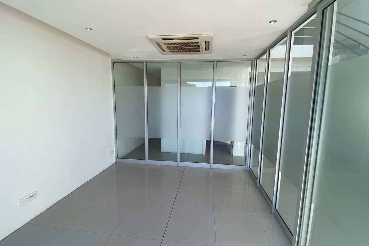 A bright, modern office space featuring tiled flooring, recessed ceiling lighting, a built-in air conditioning unit, and glass partition walls for a professional environment.